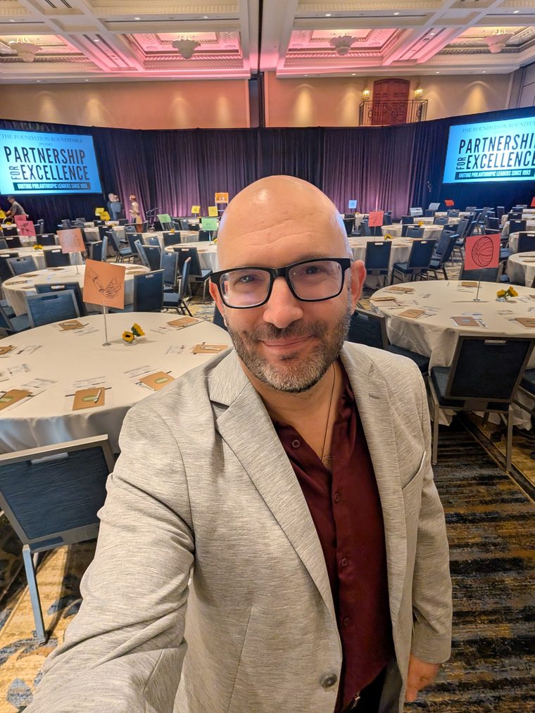Michael Kass standing in a hotel ballroom set with round tables before the conference audience arrives.