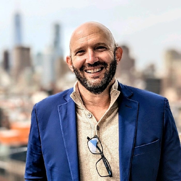 Michael Kass, smiling, with a city skyline behind him.