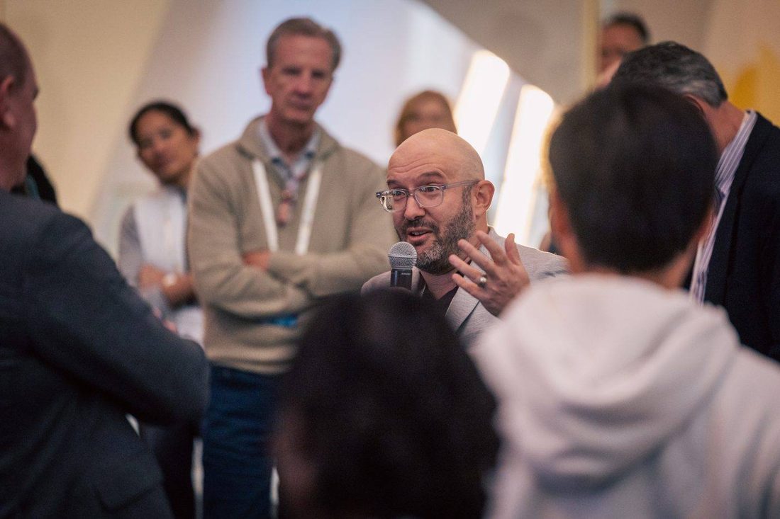 Michael Kass speaking into a handheld microphone, surrounded by a standing audience.