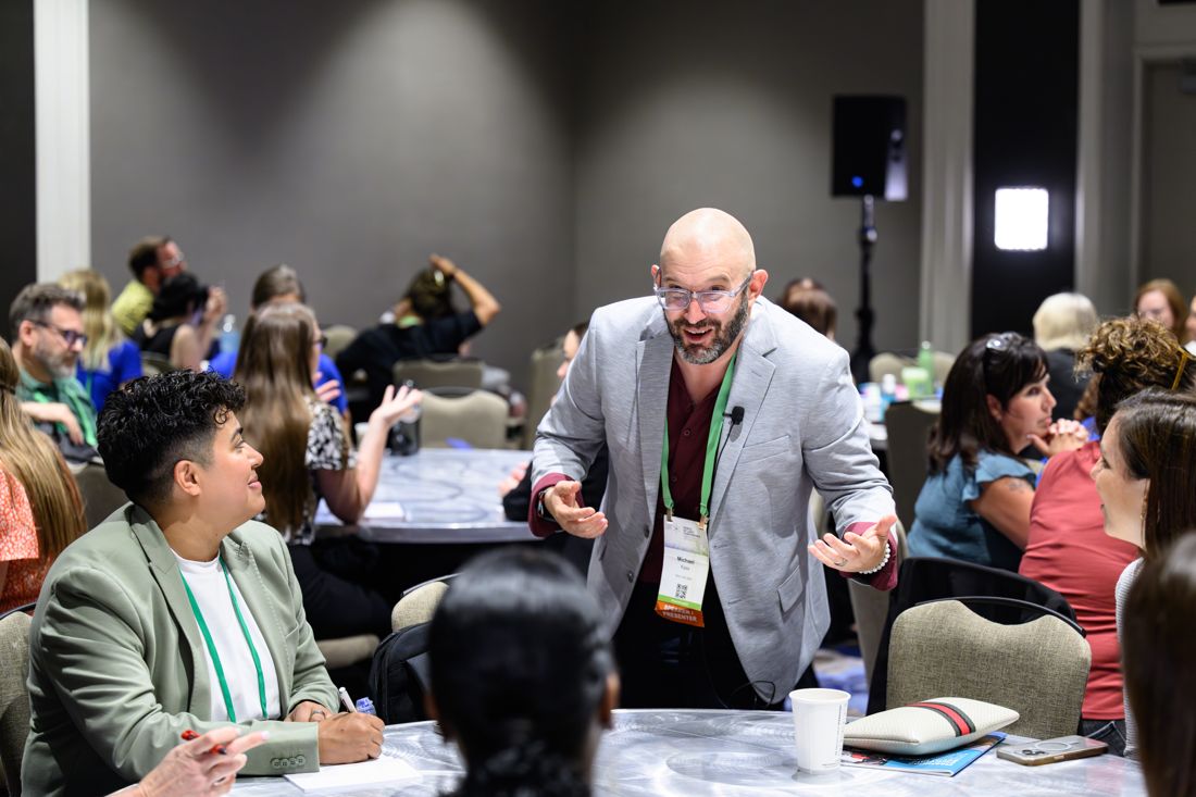 Michael Kass leaning in, mid-conversation, with participants seated at round tables during a training.